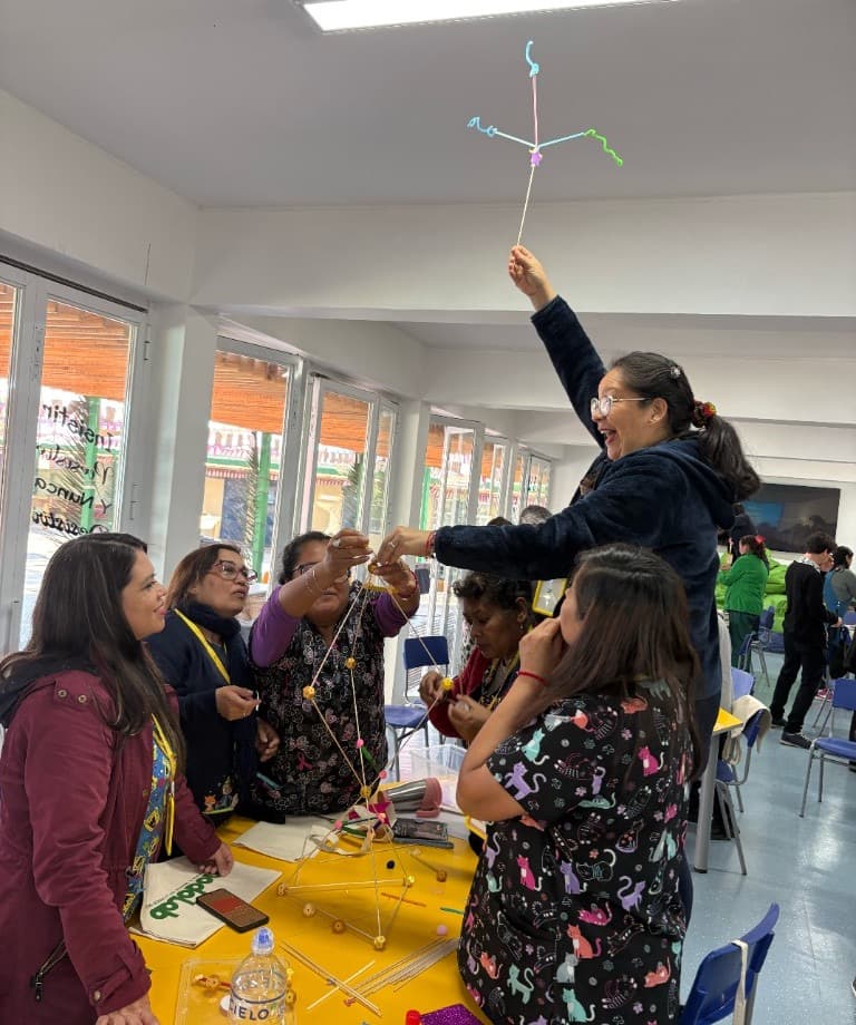 Un grupo construye una estructura en una mesa amarilla y una participante la levanta para mostrarla.