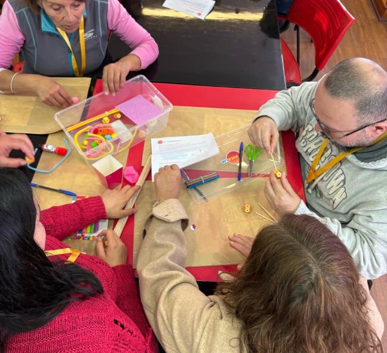 Manos de varias personas armando materiales sobre la mesa de un taller.